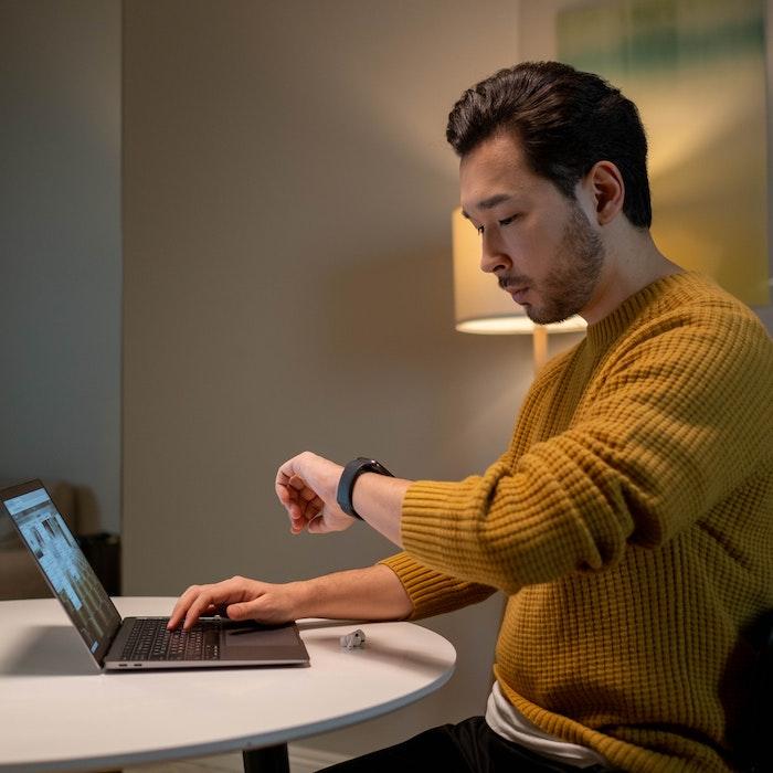 Man in Brown Sweater Looking at Time on His Smartwatch while Using Laptop