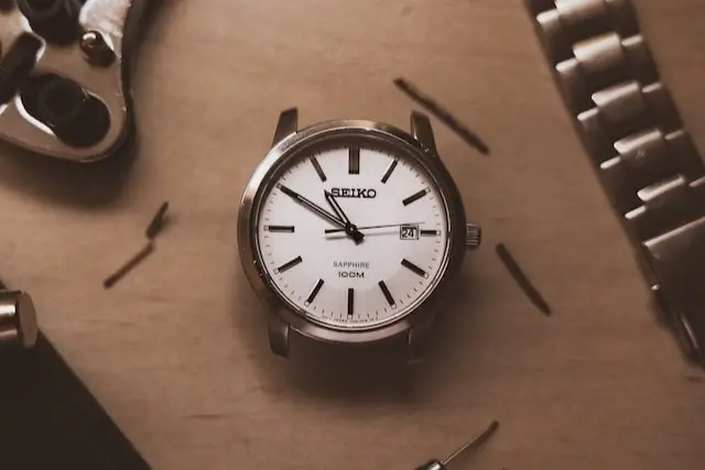 Close-up of a Seiko watch case without a bracelet, accompanied by a bracelet and a case back opener.