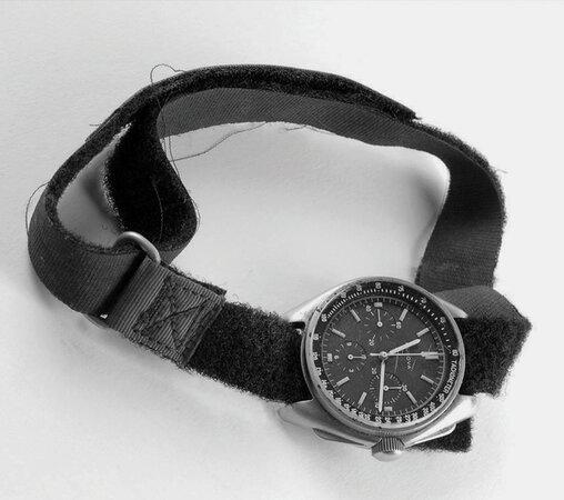 A black and white image of a vintage Bulova wristwatch with a black fabric strap and detailed chronograph face, placed on a white background.