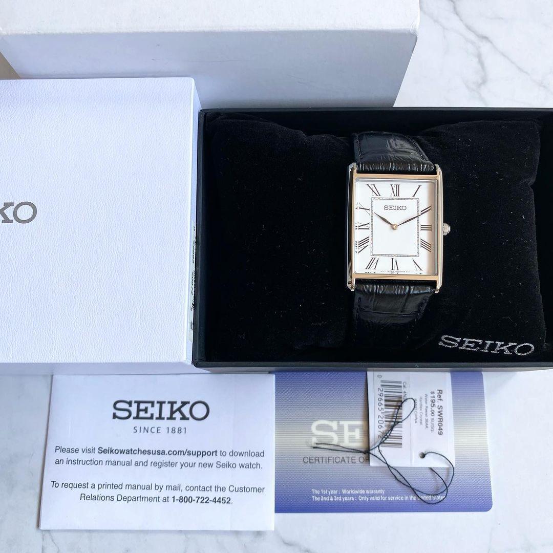 A rectangular Seiko watch with a white dial and a black leather strap, resting inside an open white box.