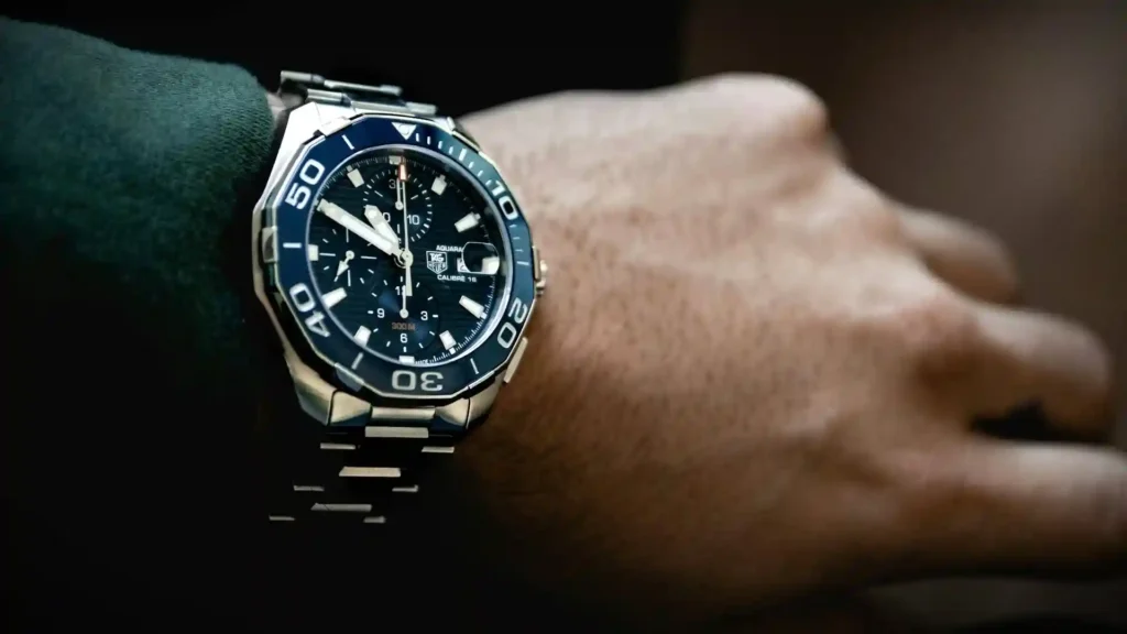 Close-up of a man's wrist showcasing a Tag Heuer watch with a striking blue dial and a polished metal bracelet.