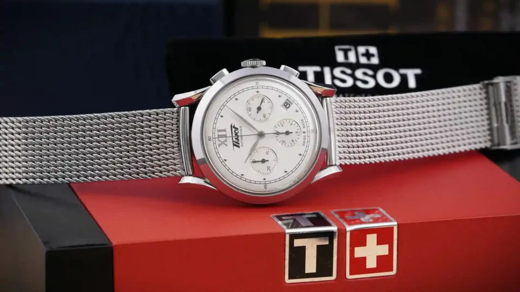 A Tissot watch with a Milanese bracelet is placed on its box.