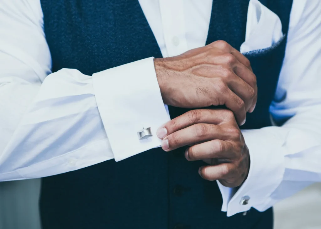 A man in a vest and tie is adjusting his cufflinks, looking sharp and ready for a formal event.