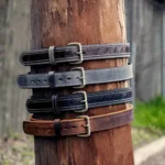 Four leather men's belts with different styles are secured to a wooden post.