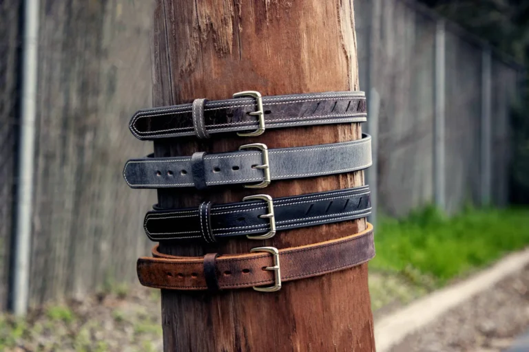 Four leather men's belts with different styles are secured to a wooden post.