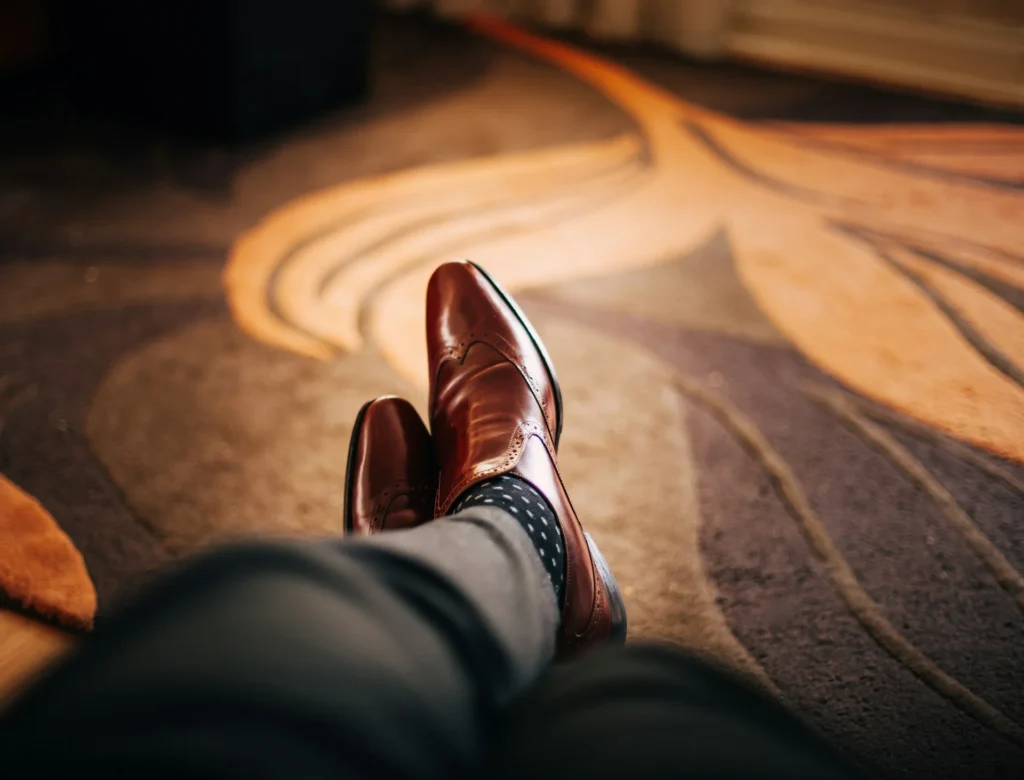 Close-up of a person's brown shoes resting on a cozy carpet.