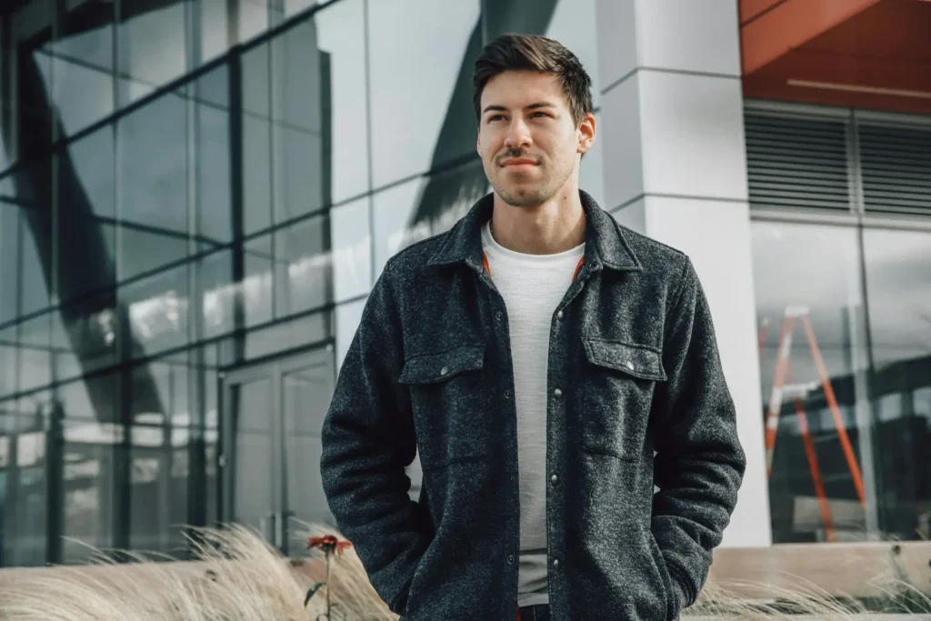 A man in a sharp suit stands before a contemporary building, highlighting his elegant fashion sense and professional appearance.