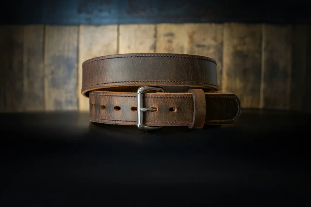 A brown leather belt laid out on a rustic wooden table.