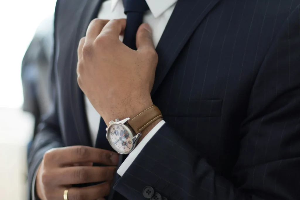 A man in a suit adjusts his tie while wearing a stylish watch on his wrist.