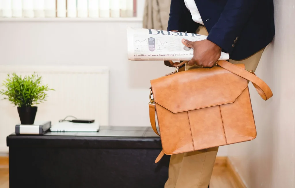 A man in a sharp suit holds a stylish brown leather bag.