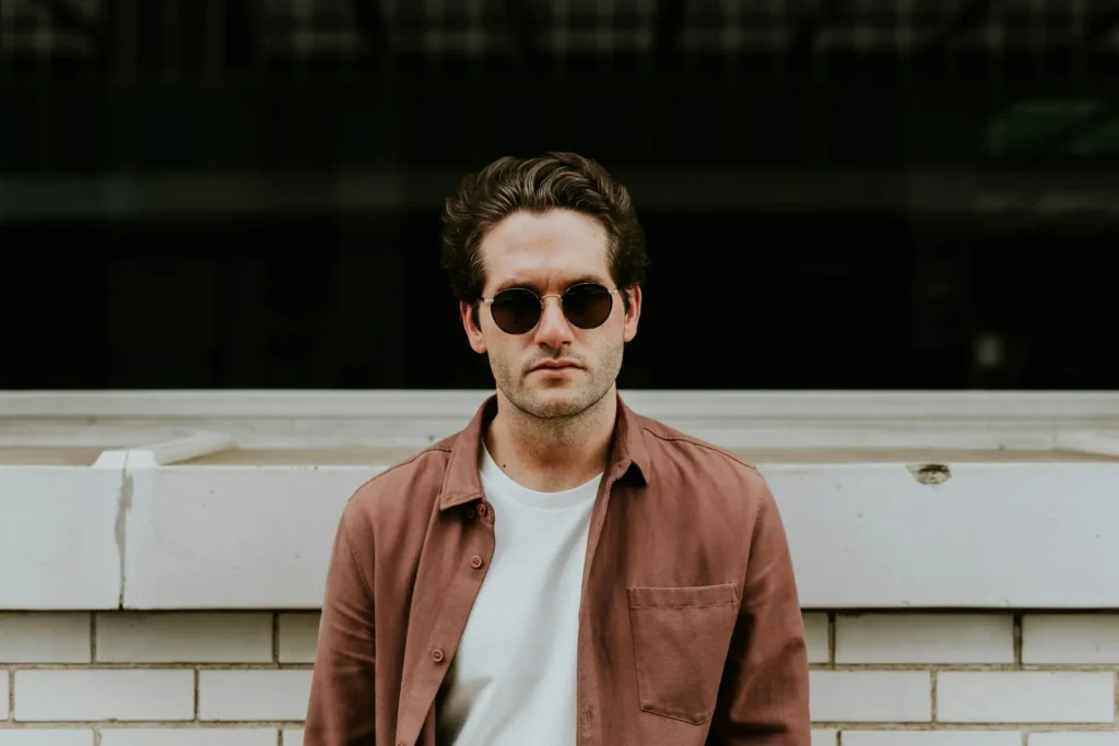  A man wearing sunglasses and a pink shirt exemplifies summer layering, presenting a fashionable and cheerful appearance.