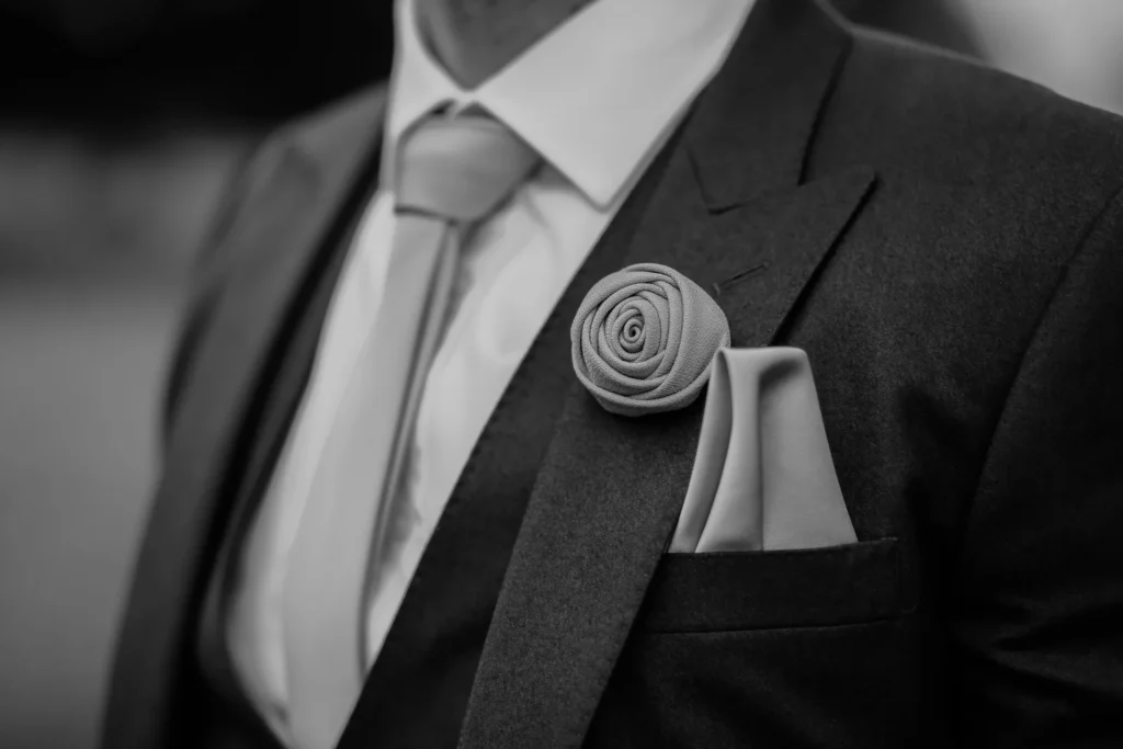 A man in a suit and tie, featuring a flower on his lapel and a stylish pocket square.