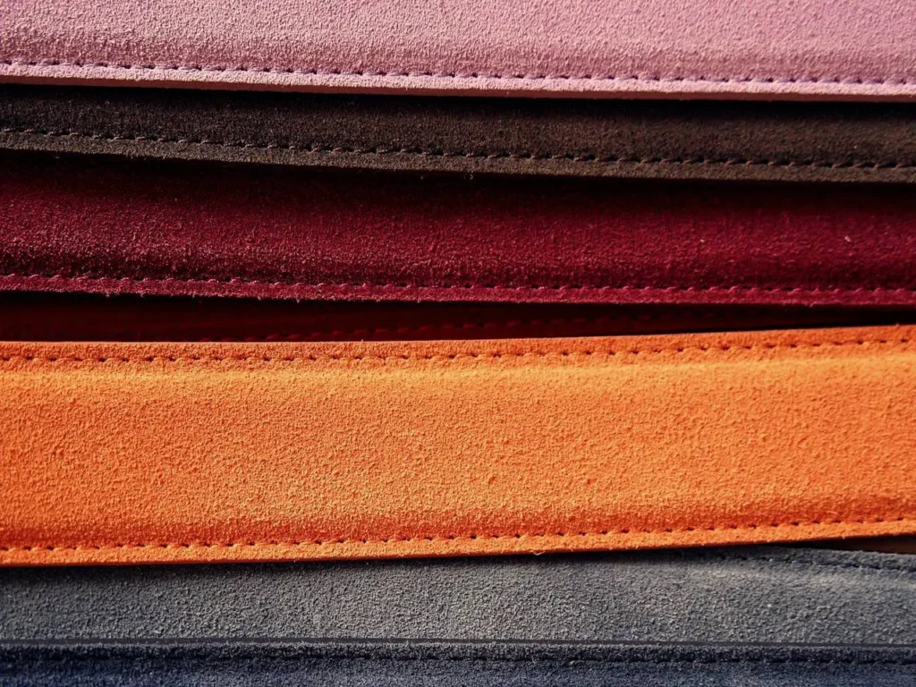 A stylish stack of men's suede belts in various colors, showcasing their texture and quality.