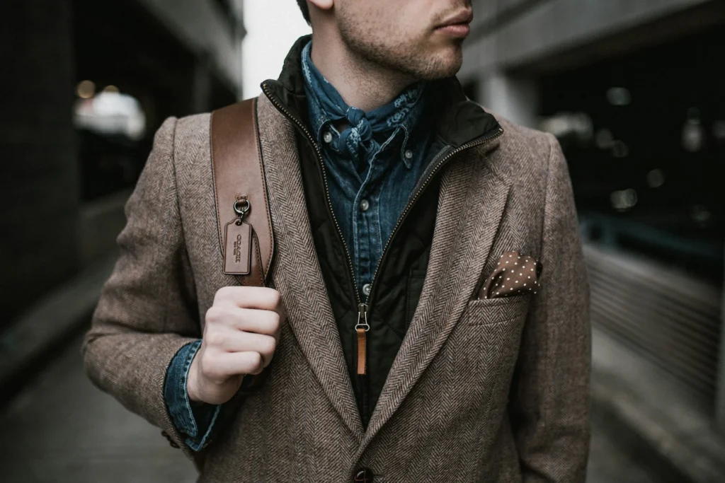 A man dressed in a suit and tie stands on the street, wearing different layers, showcasing a polished and formal appearance.