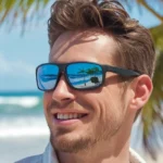 Person wearing sunglasses on a sunny beach, ocean and palm trees reflected in lenses.