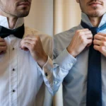 Two men in shirts and ties, one fixing his bow tie and the other adjusting his necktie, both looking sharp and dapper.