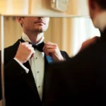 Man in tuxedo adjusting bow tie for formal event.