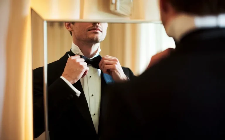 Man in tuxedo adjusting bow tie for formal event.