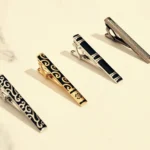 Four distinct tie clips displayed on a marble surface, showcasing various designs and finishes.