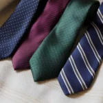 Collection of four premium silk ties in navy, burgundy, green, and charcoal-navy striped displayed diagonally on cream fabric