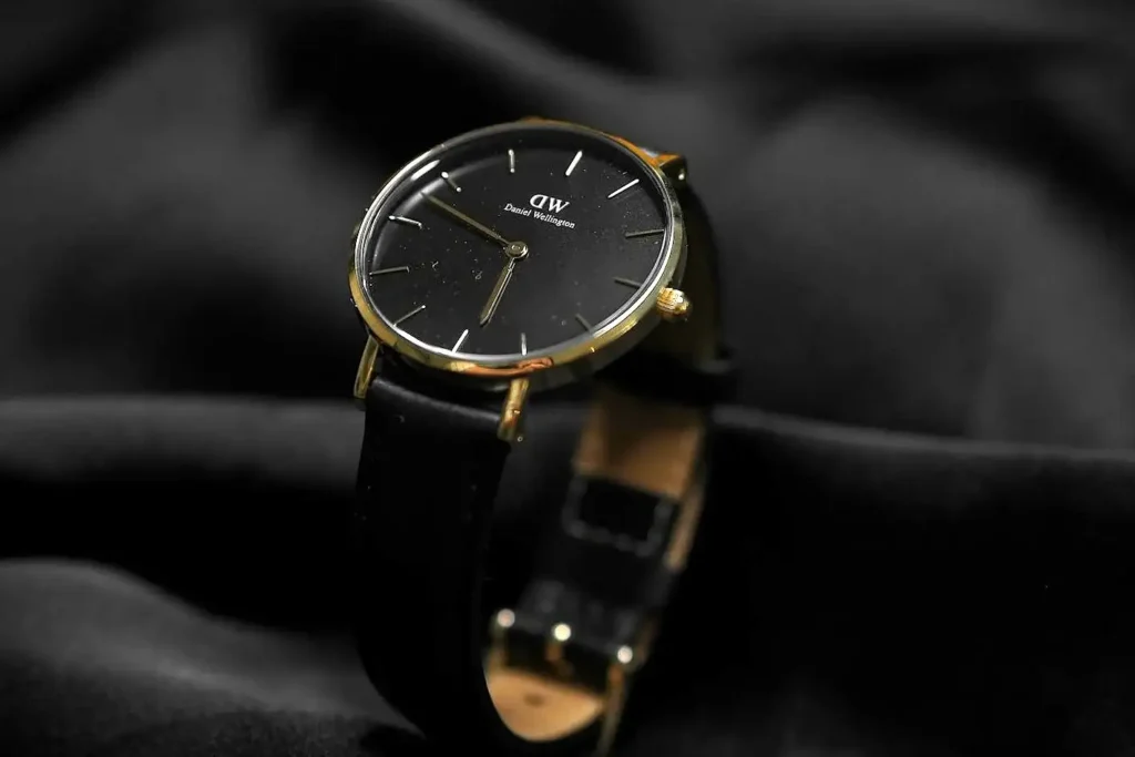 A slim Daniel Wellington watch featuring a minimalist black dial, gold-tone case, and black leather strap