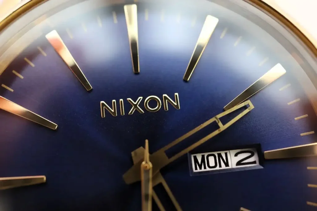 Close-up view of a Nixon watch featuring a golden brand name displayed prominently on a blue dial