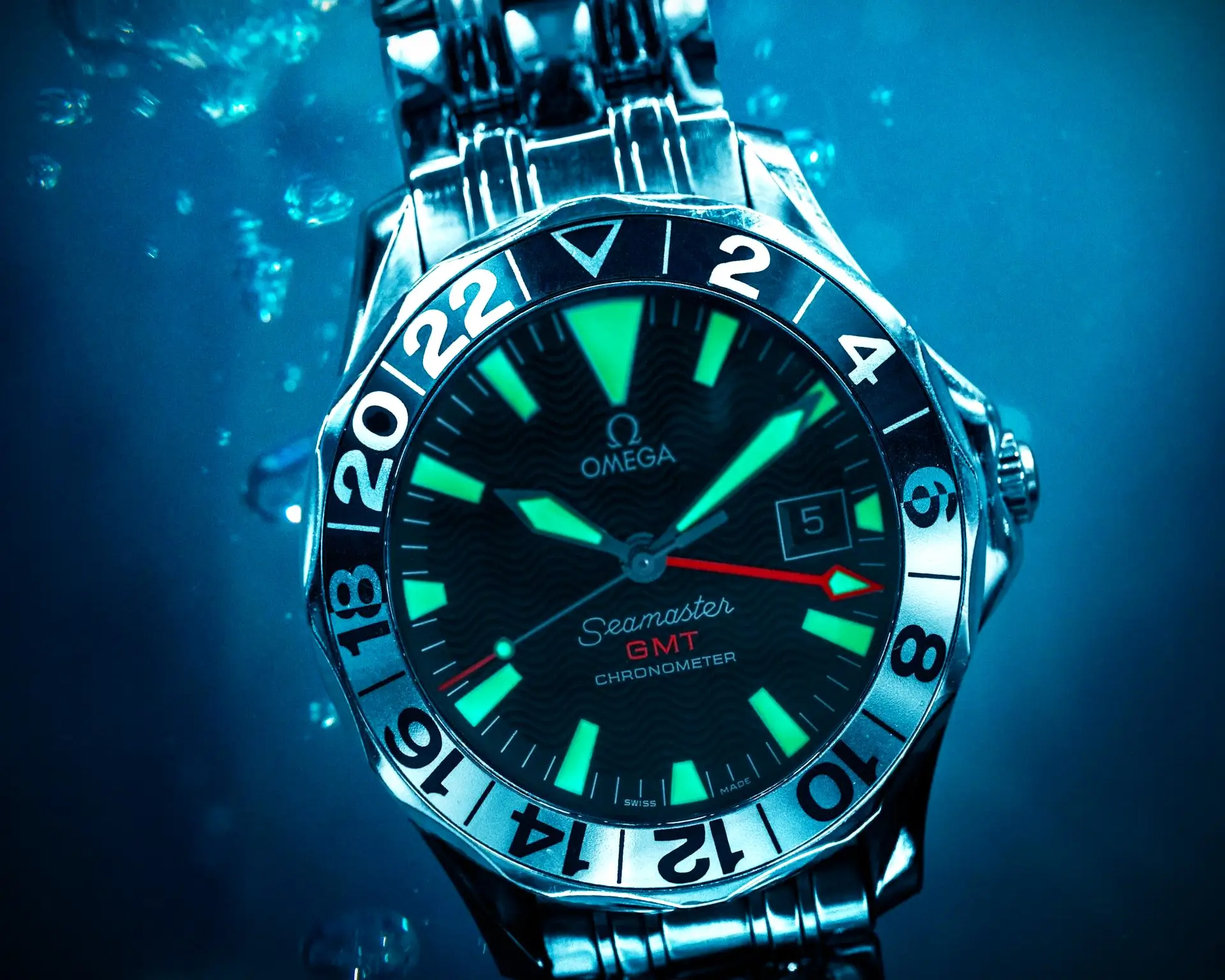 Close-up of an Omega Seamaster GMT underwater with luminous indices and hands