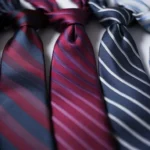 Close-up of five silk ties in navy, burgundy, red, charcoal, and silver, arranged side by side on a white background.