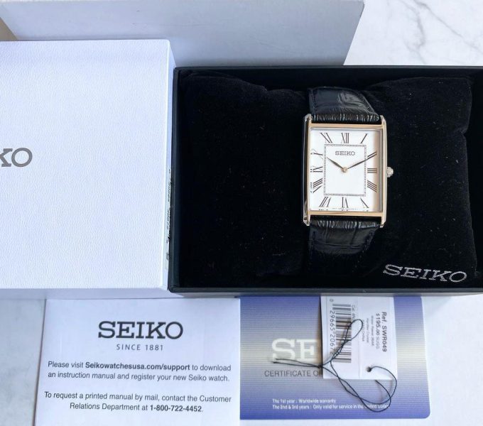 A rectangular Seiko watch with a white dial and a black leather strap, resting inside an open white box.