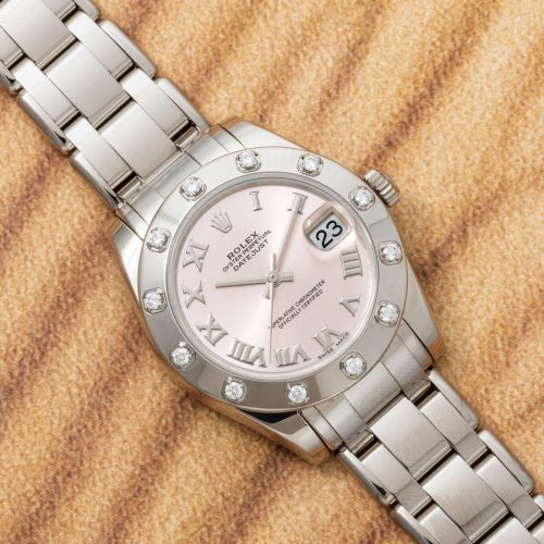 A Rolex Datejust watch with a Pearlmaster bracelet, a pink dial, Roman numerals, diamond hour markers, and a date window, positioned on a textured beige background.